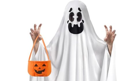 Child wearing a white friendly ghost Halloween costume, smiling and holding a pumpkin-shaped candy bucket for trick-or-treating.